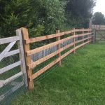 Commercial fence and gate surrounding a field. The fence is of a post and rail style perfect for a rural look.