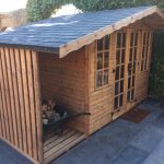 Made to measure garden shed in a garden. This bespoke shed has a slate roof and a log store on the side.