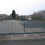 Green steel palisade gates stand in front of an empty yard. These commercial gates are perfect for securing school yards.