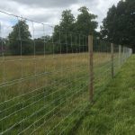 A long fence with round fence posts. The fence stands on a empty field.