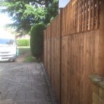 A wooden fence next to a large vehicle. It is a v type fence with close board fence panels.